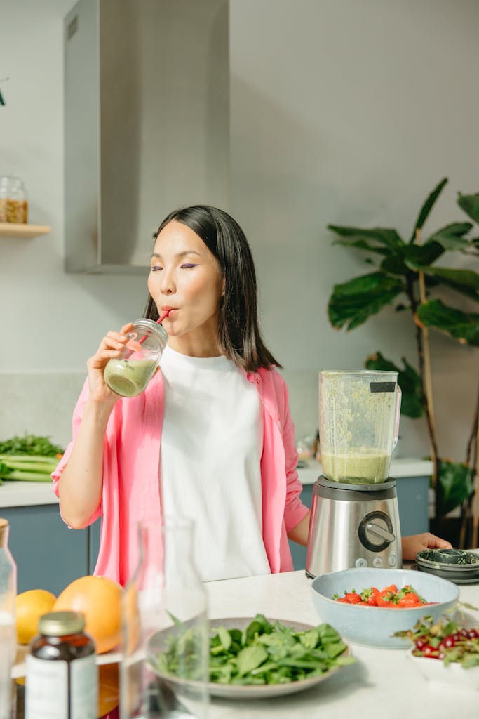 Asian woman sipping a green smoothie in a modern kitchen setting. Detox