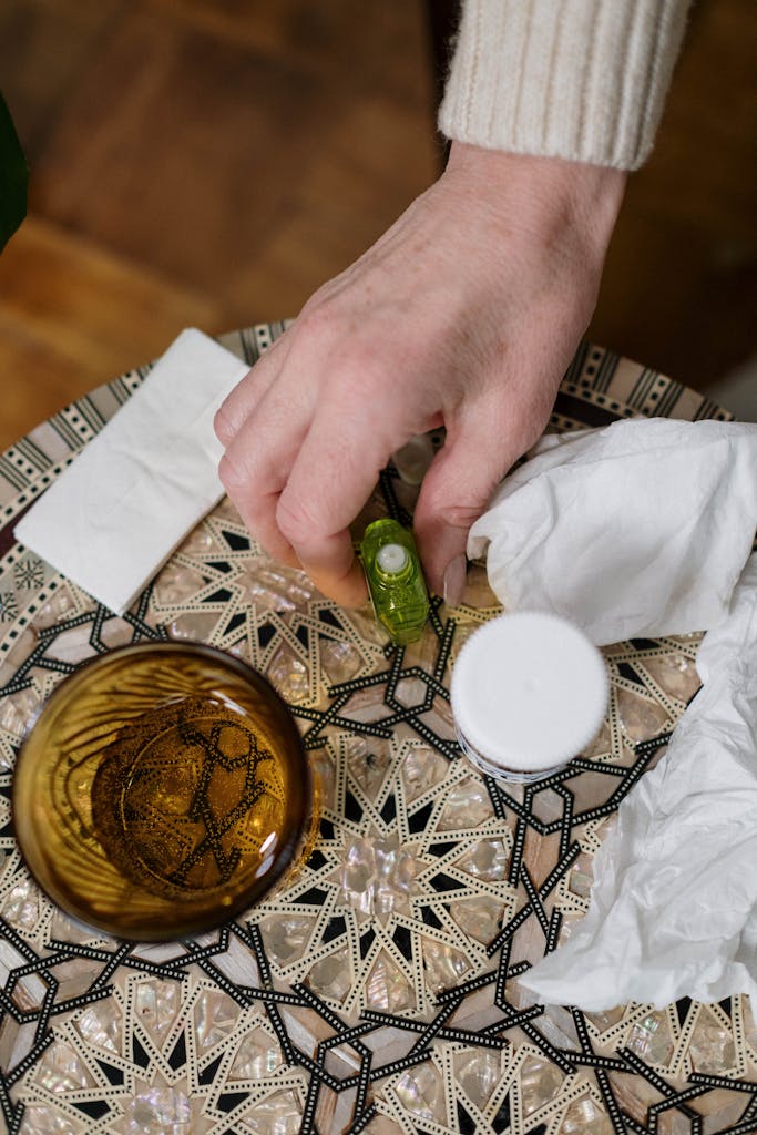 Close-up of a hand reaching for medicine on a patterned table with tissues nearby.