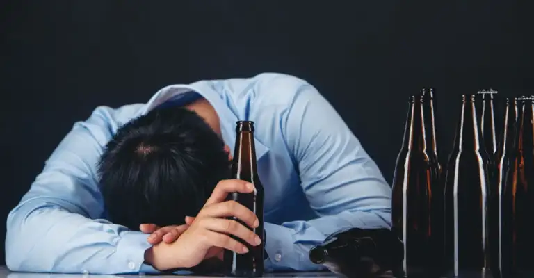 Man struggling with alcohol addiction surrounded by empty beer bottles affecting relationships and work performance