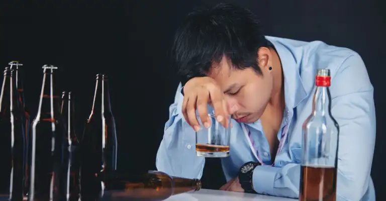 Man struggling with alcohol addiction and anxiety sitting with empty bottles in a distressed state