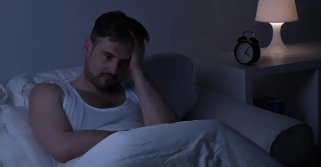 Man lying awake at night struggling with insomnia caused by alcohol and anxiety