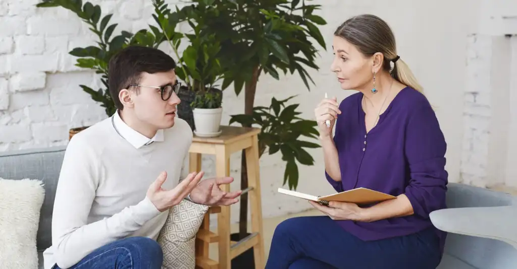 Young man discussing anxiety and alcohol addiction with therapist during counselling session